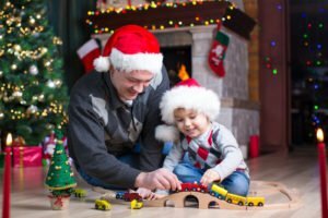 Father with his son play with model railway near christmas tree